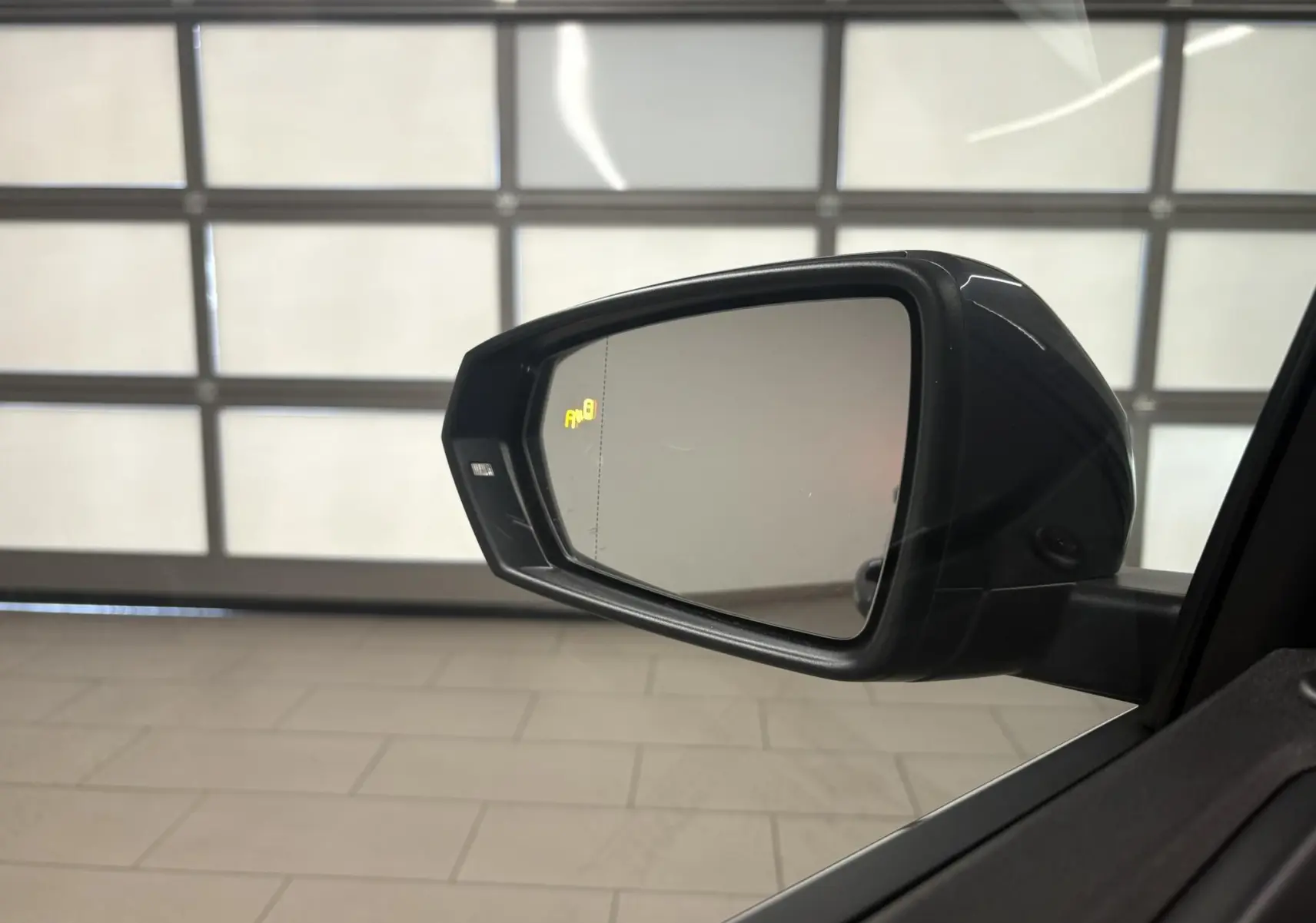Rétroviseur extérieur droit de Volkswagen Polo gris cendré 2025 avec indicateur d'angle mort allumé.