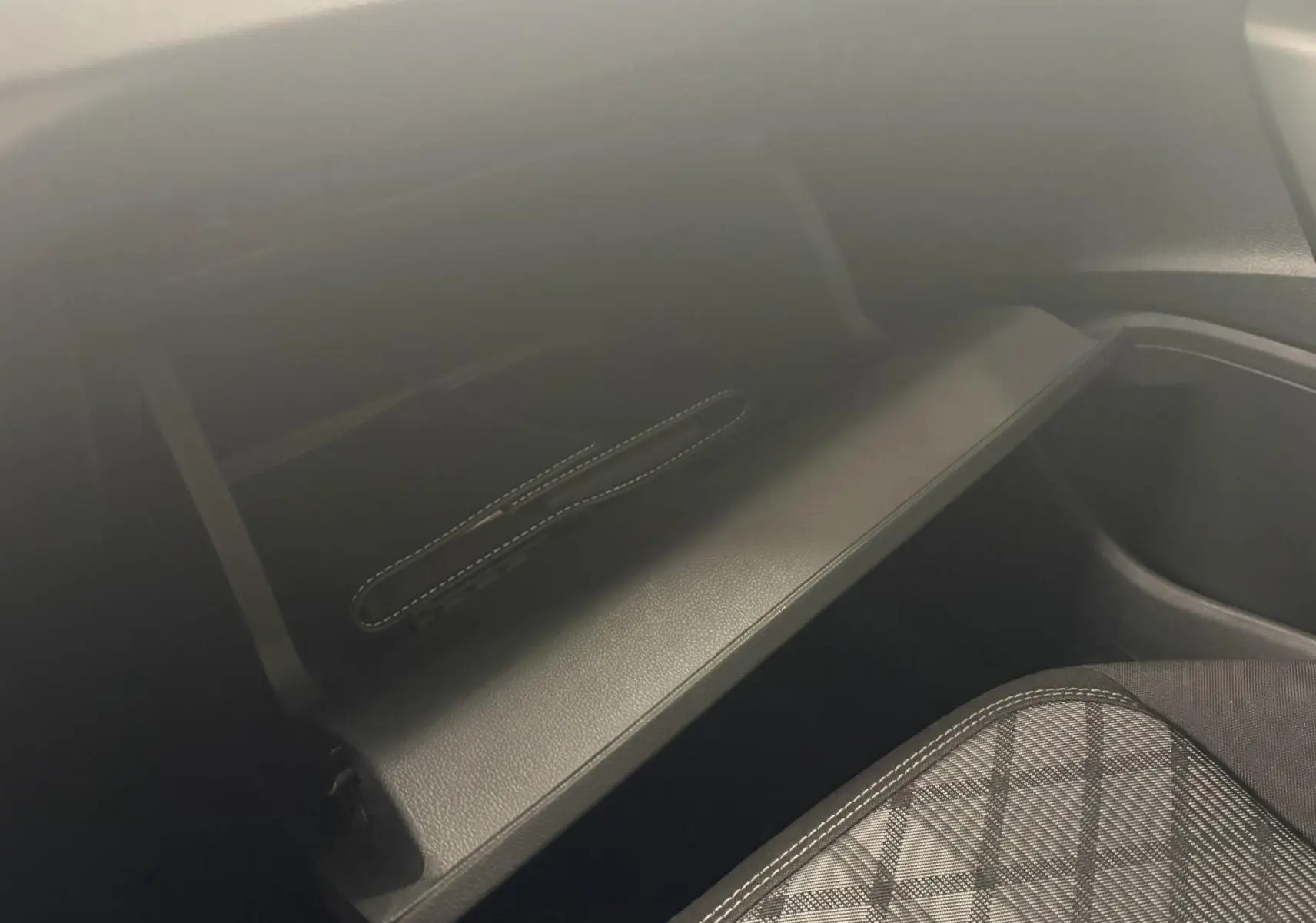 Intérieur du Volkswagen Polo 2025, vue sur la boîte à gants ouverte et siège avant avec tissu à motif écossais.
