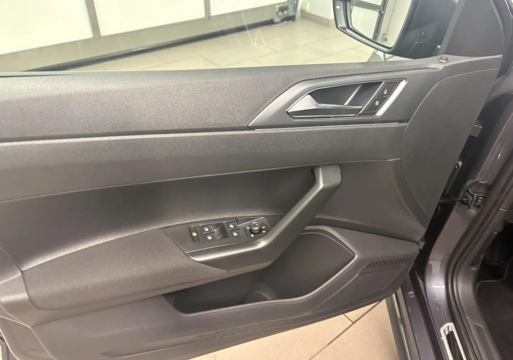 Vue rapprochée de la porte avant gauche intérieure d'une Volkswagen Polo gris cendré avec commandes de vitres et serrure.