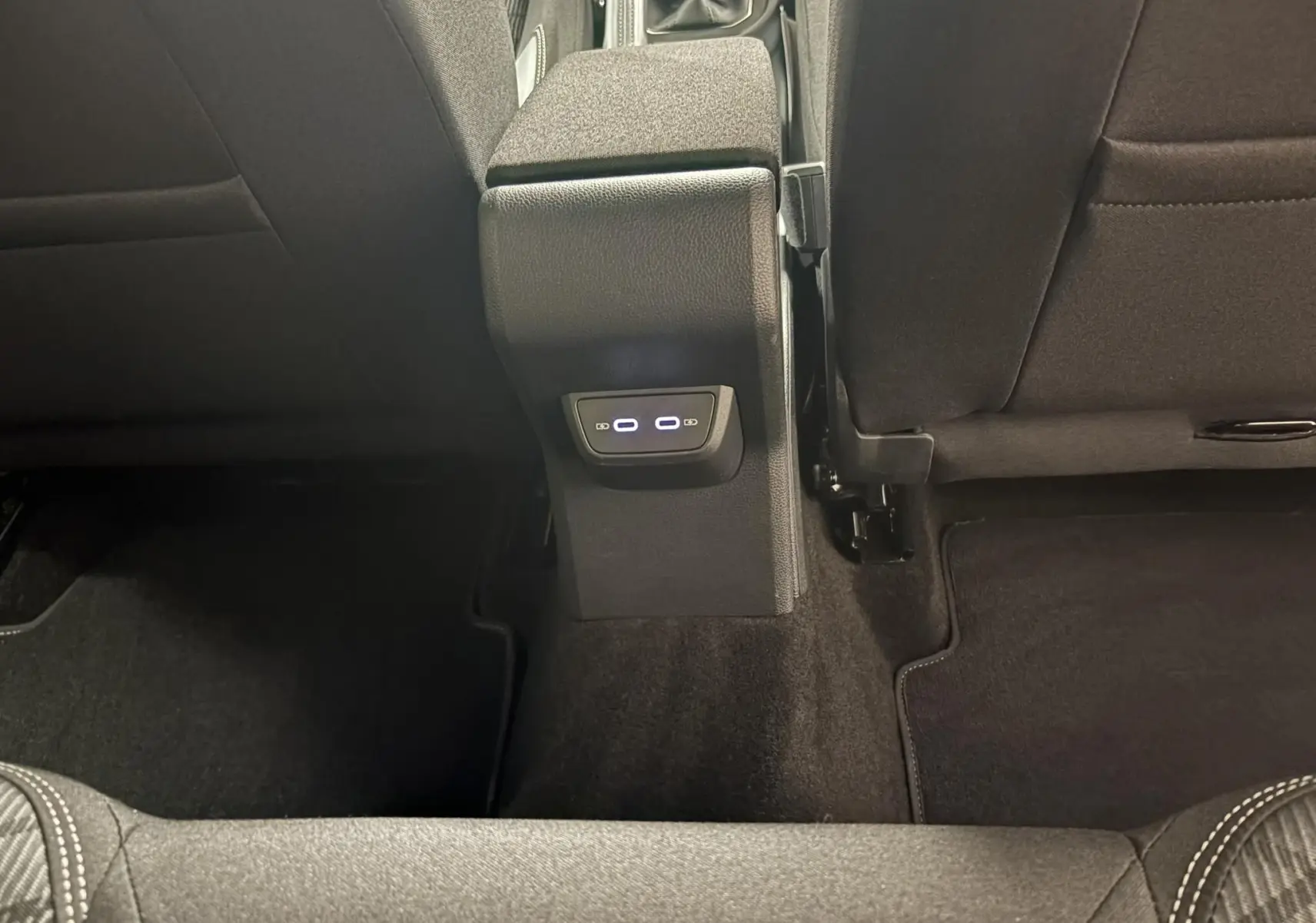 Vue intérieure arrière centrée sur la console centrale avec ports USB illuminés, sièges en tissu gris foncé.