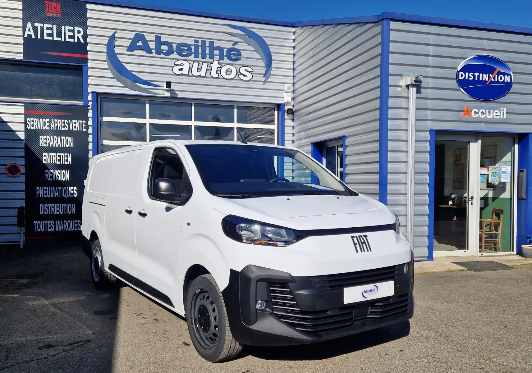 Fourgon FIAT Scudo blanc en 3/4 avant droit, avec pare-chocs noir et calandre moderne, stationné devant un garage.