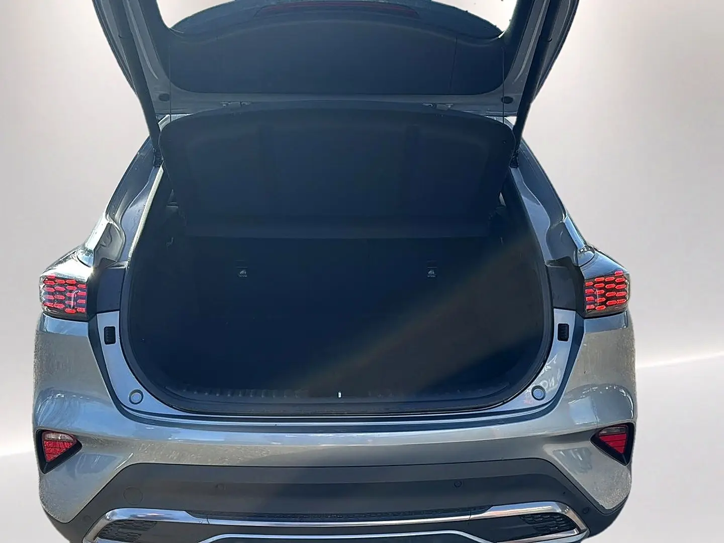 Vue arrière du coffre ouvert d'un KIA Xceed gris 2024 avec feux arrière LED allumés et pare-chocs chromé.