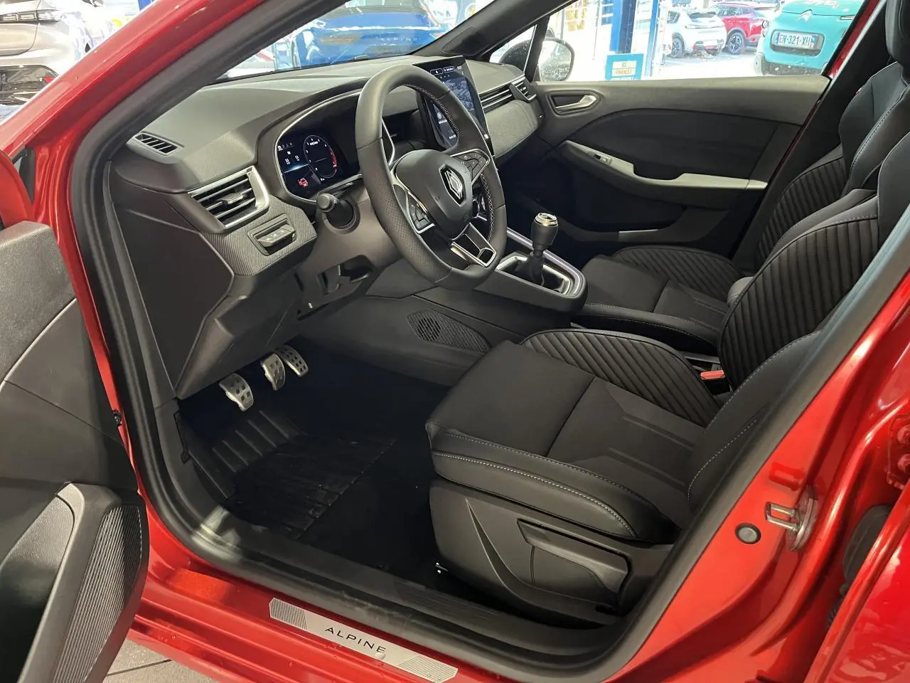 Intérieur côté conducteur de Renault Clio 2024 rouge, volant multifonction, sièges tissu noir avec surpiqûres Alpine.