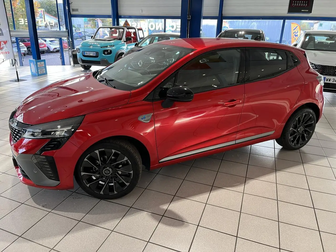 Renault Clio 2024 rouge vue de profil côté gauche, avec jantes noires et badge Esprit Alpine sur aile avant.