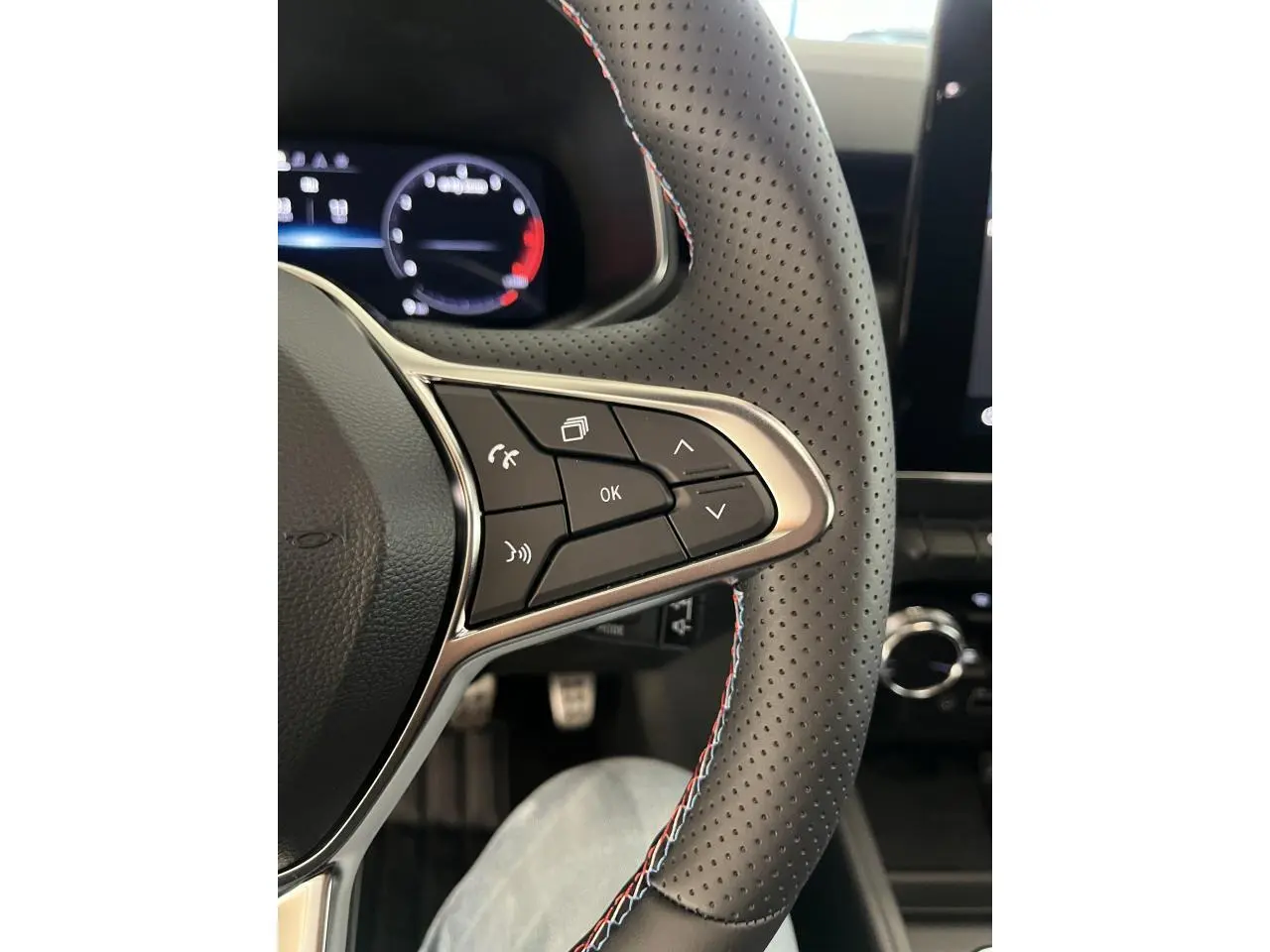 Gros plan sur le volant perforé noir avec surpiqûres tricolores et commandes multifonctions de la Renault Clio Esprit Alpine 2024.