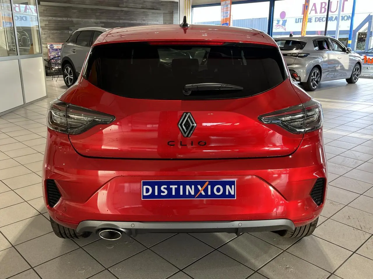Vue arrière d'une Renault Clio rouge 2024 avec logo et échappement chromé en concession.