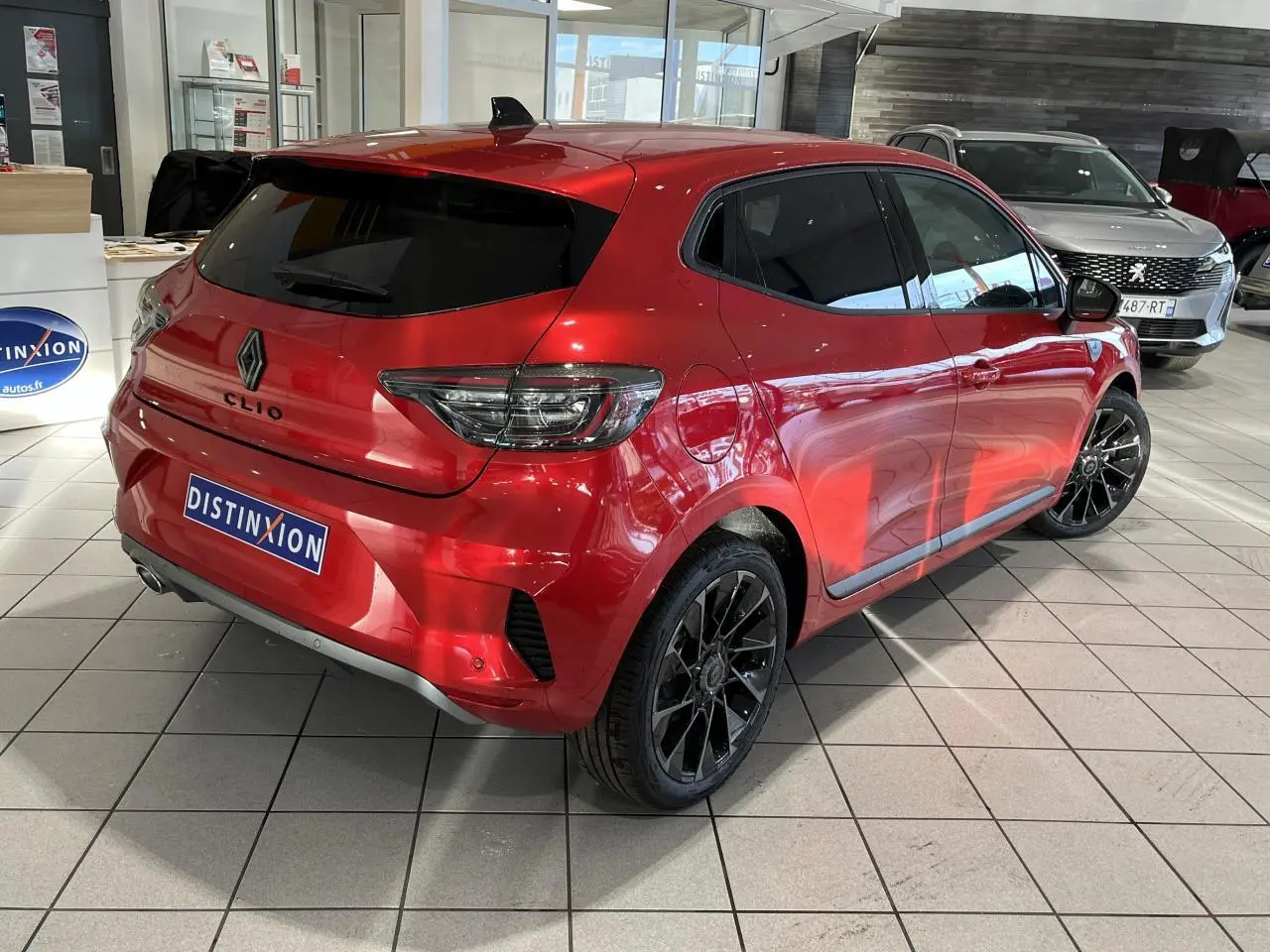 Renault Clio 2024 rouge vue 3/4 arrière droit en showroom avec jantes noires et feux LED en C.