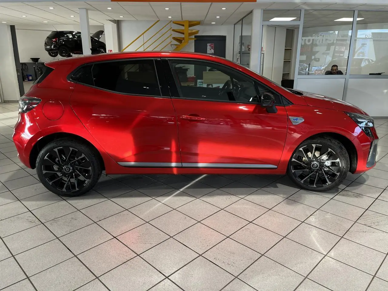 Profil droit d'une Renault Clio 1.0 Tce 90 Esprit Alpine rouge avec jantes noires et badge Alpine sur aile avant.