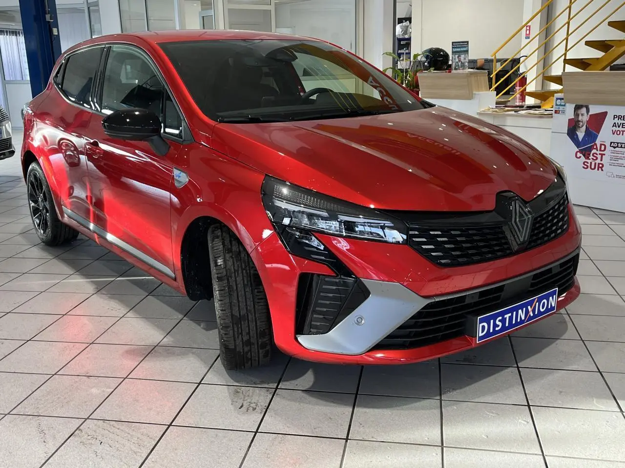 Renault Clio 2024 rouge vue 3/4 avant avec calandre noire et détails gris schiste satin.