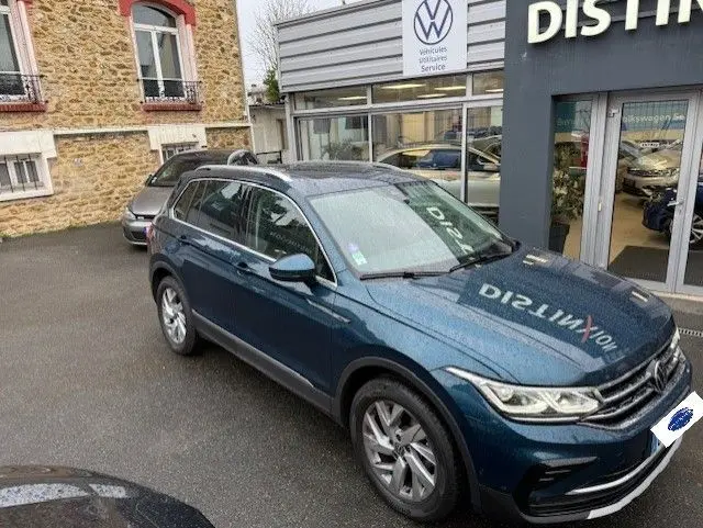 Volkswagen Tiguan 2022 bleu nuit en 3/4 avant droit devant un concessionnaire avec toit panoramique et jantes alliage.