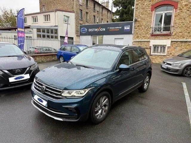 Volkswagen Tiguan 2022 bleu Night Shade en 3/4 avant droit sur parking urbain, avec jantes alliage visibles.