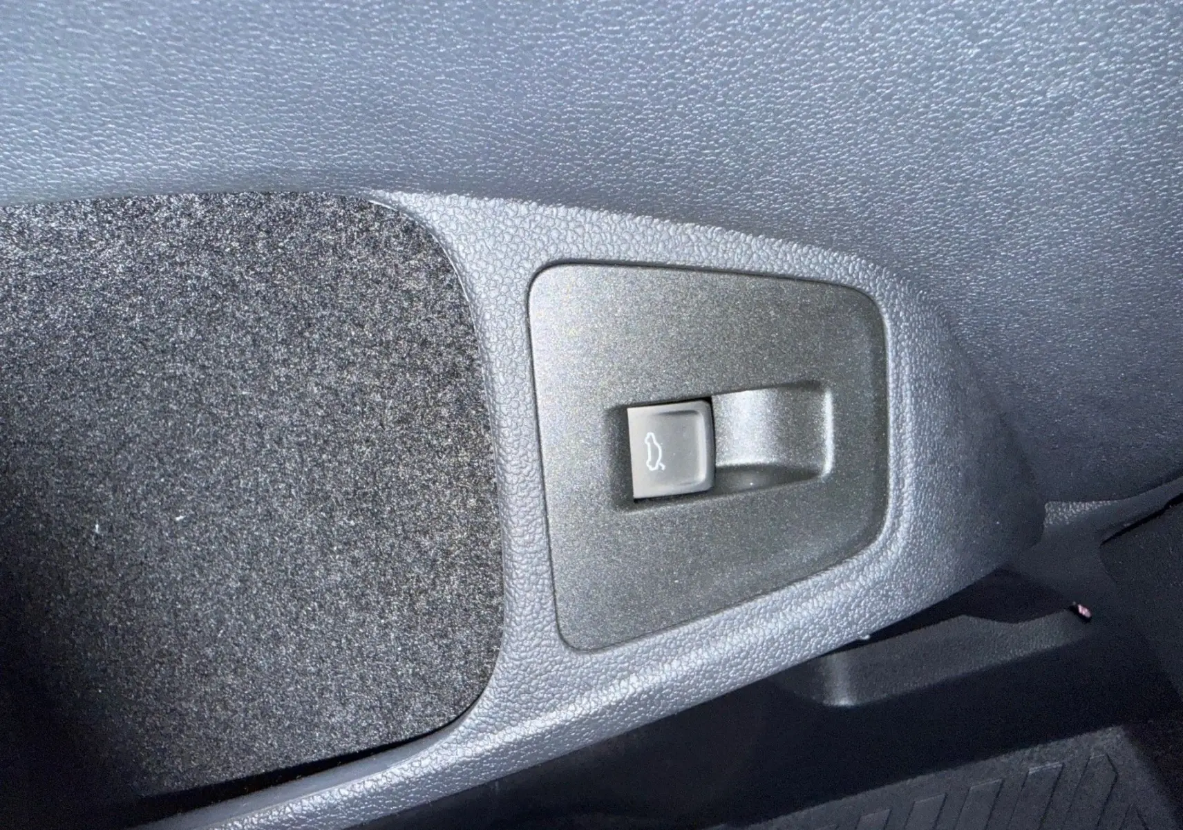Bouton d'ouverture du coffre en plastique noir sur le revêtement intérieur gris foncé du Volkswagen Tiguan 2022.