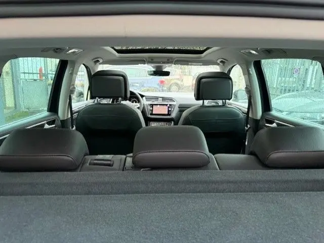 Vue intérieure arrière du Volkswagen Tiguan 2022, sièges cuir noir et toit ouvrant panoramique visibles.
