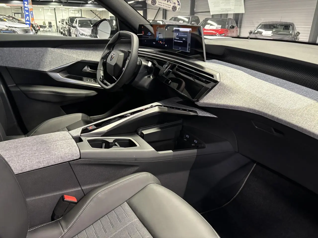 Intérieur avant droit du Peugeot 3008 Hybrid 2025 avec tableau de bord tissu gris clair et écran panoramique incurvé.