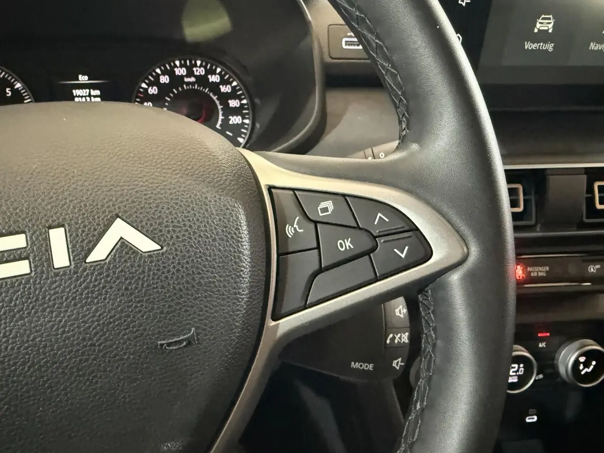 Gros plan sur le volant en cuir synthétique de la Dacia Sandero 2024, avec commandes multifonctions visibles côté droit.