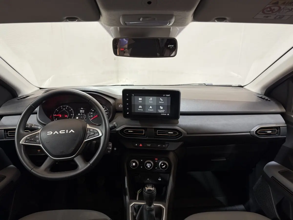 Vue frontale de l'intérieur du Dacia Sandero 2024 avec volant cuir multifonctions et écran tactile central.