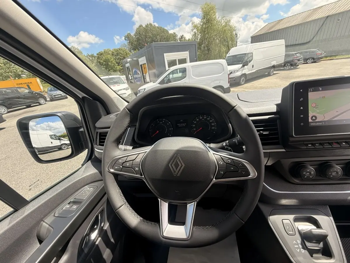 Vue intérieure centrée sur le volant multifonctions noir du Renault Trafic Fourgon blanc, avec tableau de bord et écran tactile visibles.