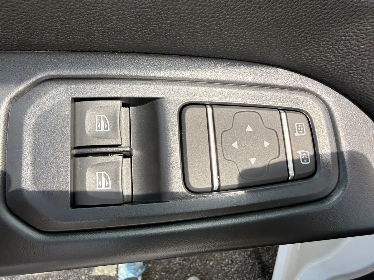 Gros plan sur les commandes de réglage des vitres et des rétroviseurs côté conducteur du Renault Trafic Fourgon blanc.