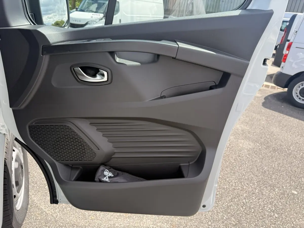 Vue rapprochée de la porte avant droite blanche du Renault Trafic Fourgon, montrant la poignée et le rangement intégré.