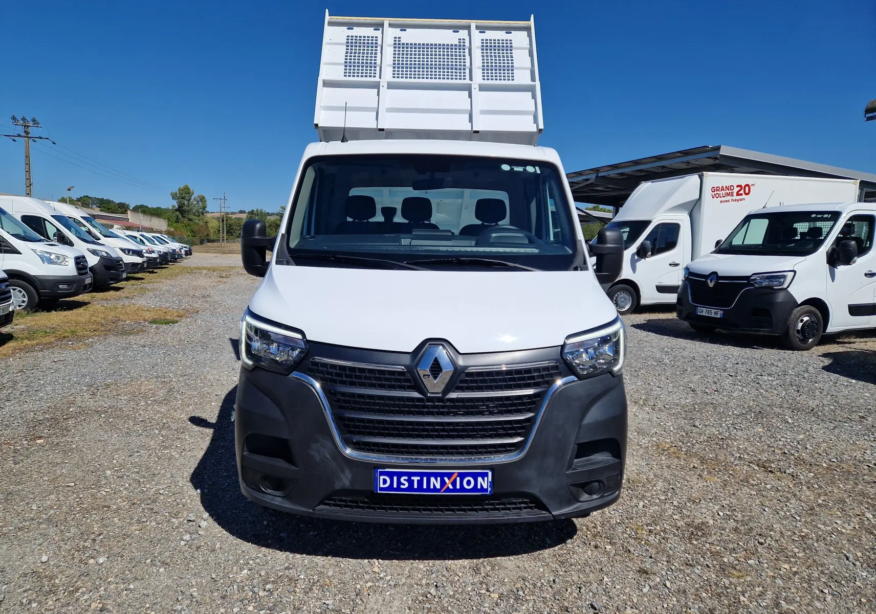 Vue frontale d’un Renault Master Châssis Cabine blanc avec benne sur un parking en extérieur sous ciel bleu.