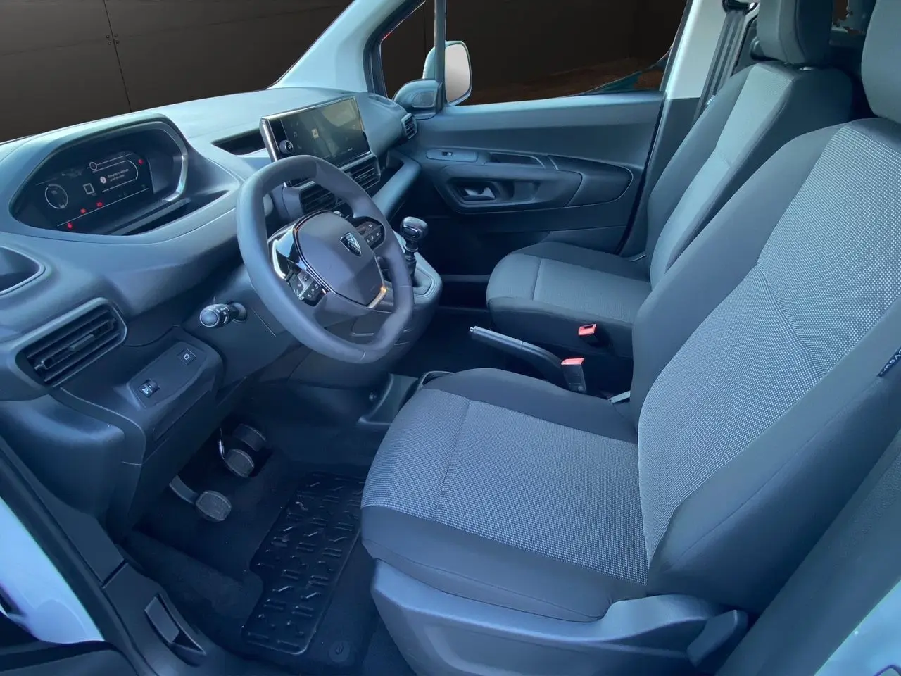 Intérieur côté conducteur du Peugeot Partner 2024 blanc, avec tableau de bord moderne et sièges tissu gris noir.