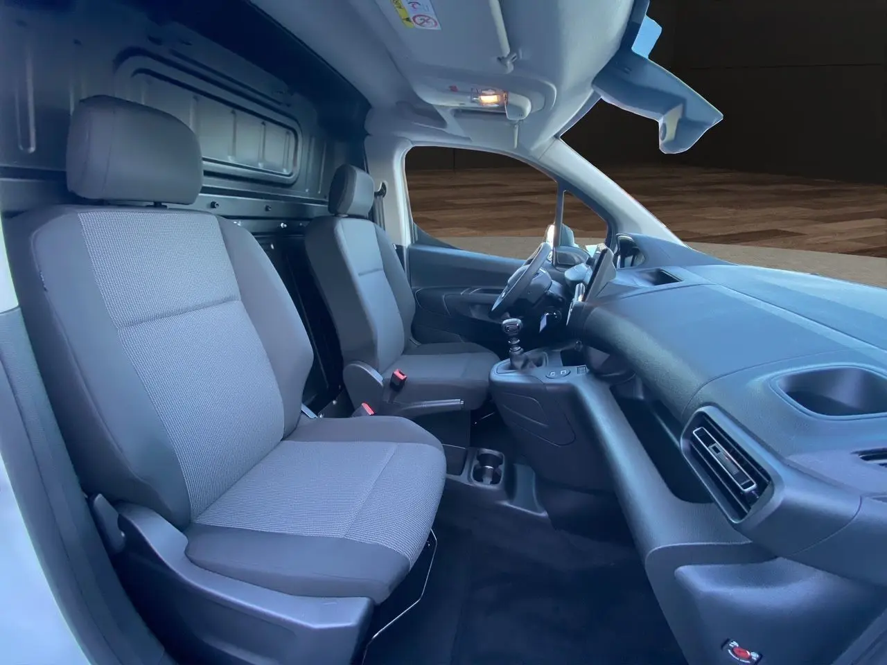 Intérieur du Peugeot Partner 2024 vu côté conducteur, sièges tissu gris et tableau de bord noir simple.