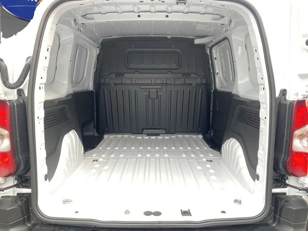 Vue arrière du coffre blanc du Peugeot Partner 2024, montrant l'espace de chargement vide avec parois noires et plancher métallique.