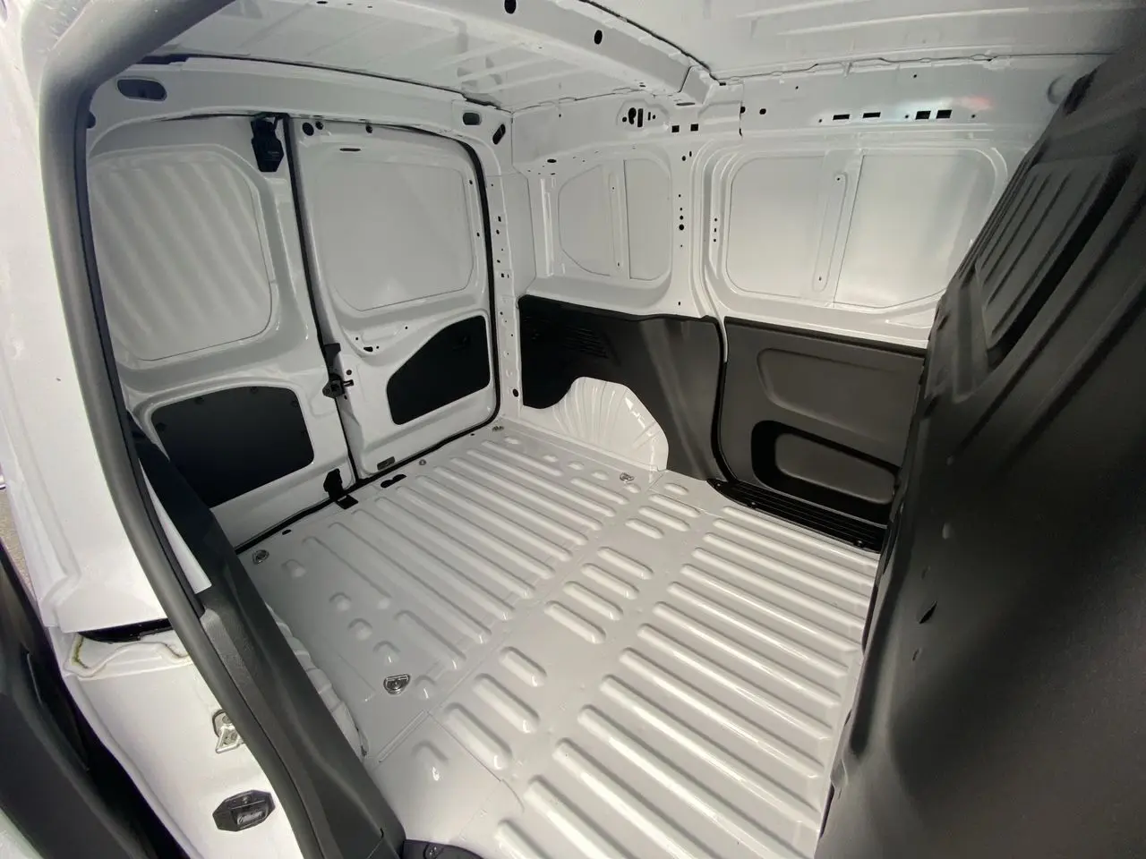 Vue intérieure de la partie arrière du Peugeot Partner blanc 2024, montrant la zone de chargement vide avec parois métalliques.