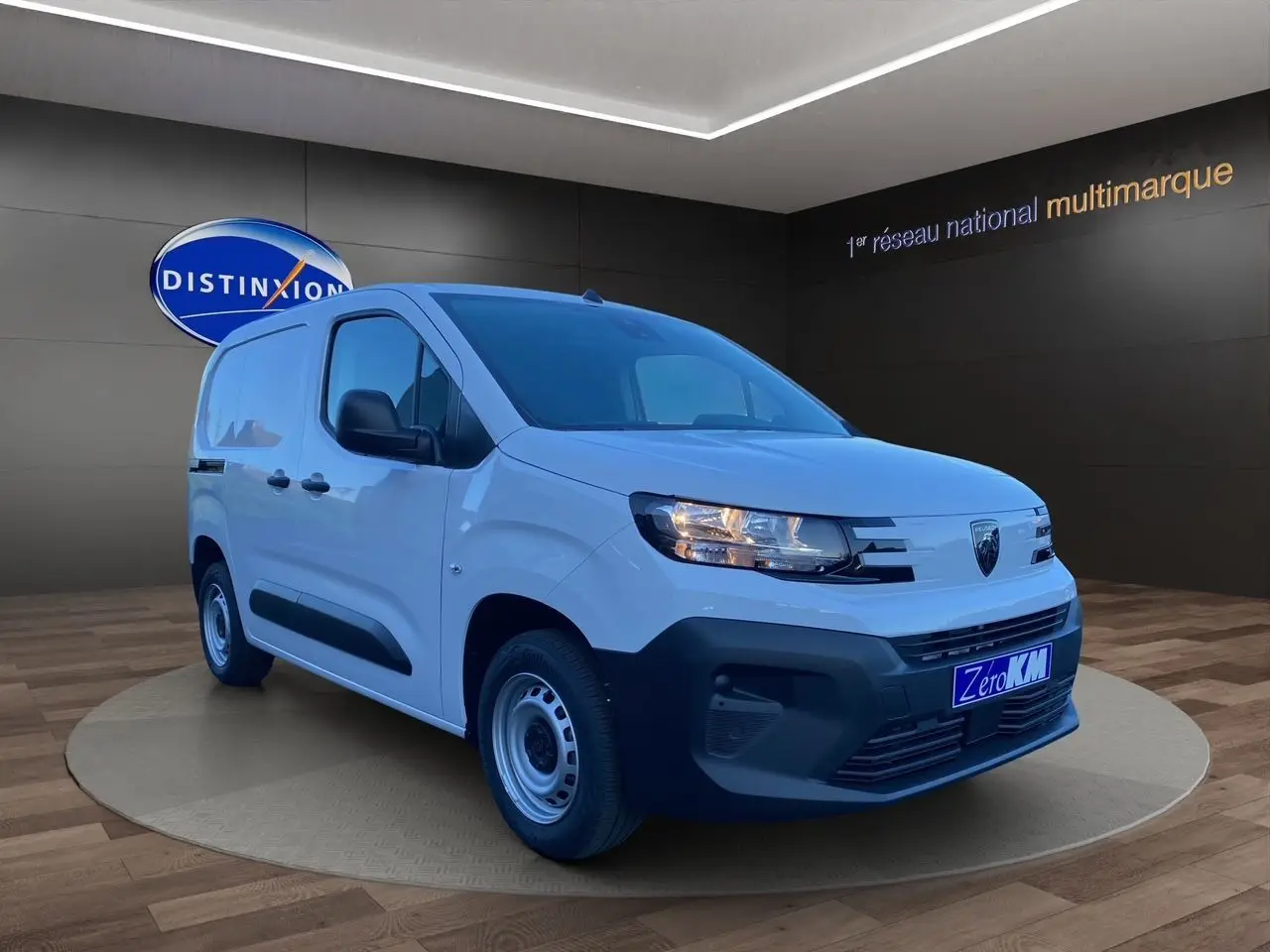 Peugeot Partner blanc en 3/4 avant droit, avec pare-chocs noir et jantes acier, en showroom intérieur.