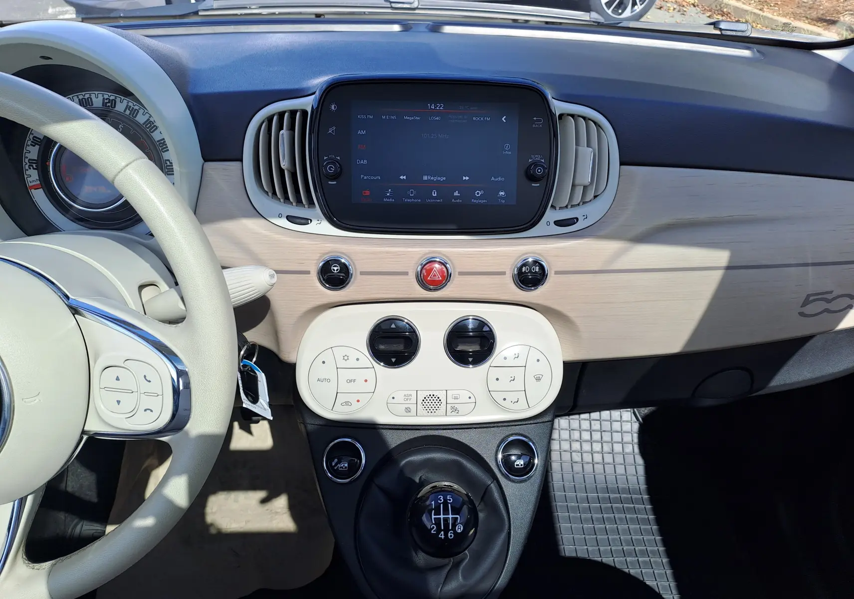 Vue intérieure du tableau de bord beige clair et noir de la Fiat 500 1.0 Hybrid 2022 avec levier de vitesse manuel et écran tactile central.