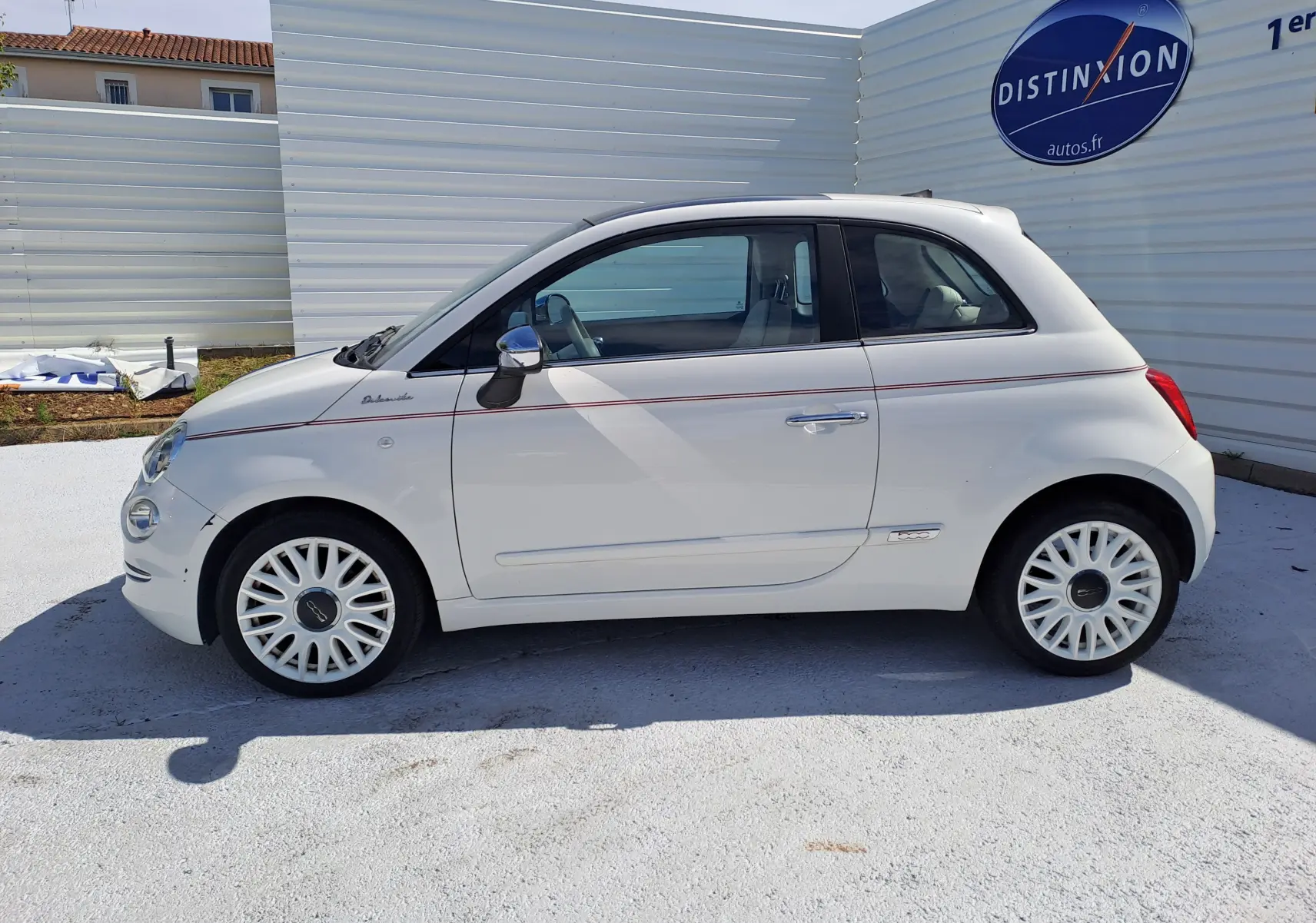 Profil côté droit d'une FIAT 500 blanche 2022 avec ligne rouge fine et jantes blanches ajourées, stationnée en extérieur.