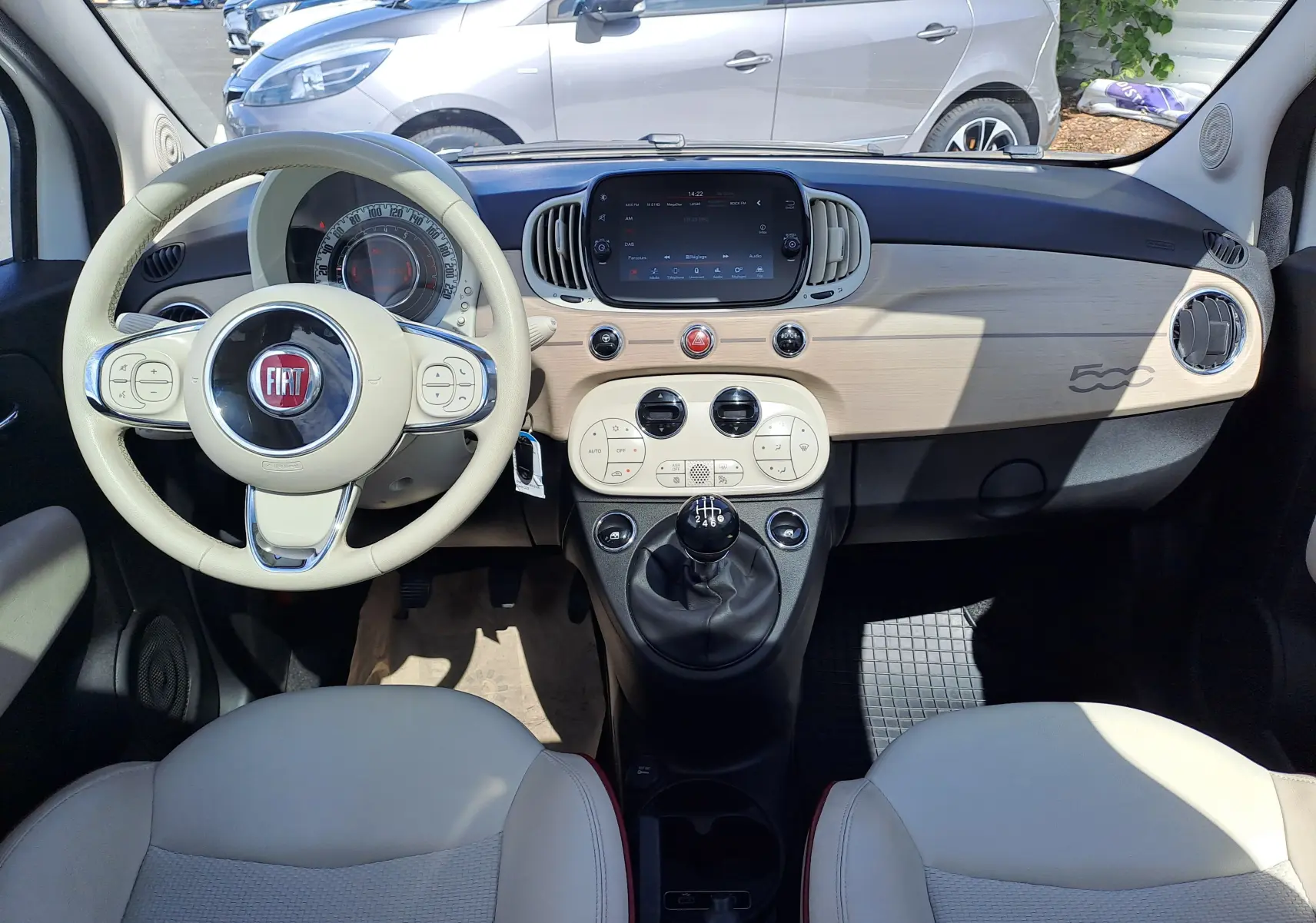 Vue intérieure avant de la Fiat 500 blanche 2022 avec tableau de bord beige clair et volant assorti.