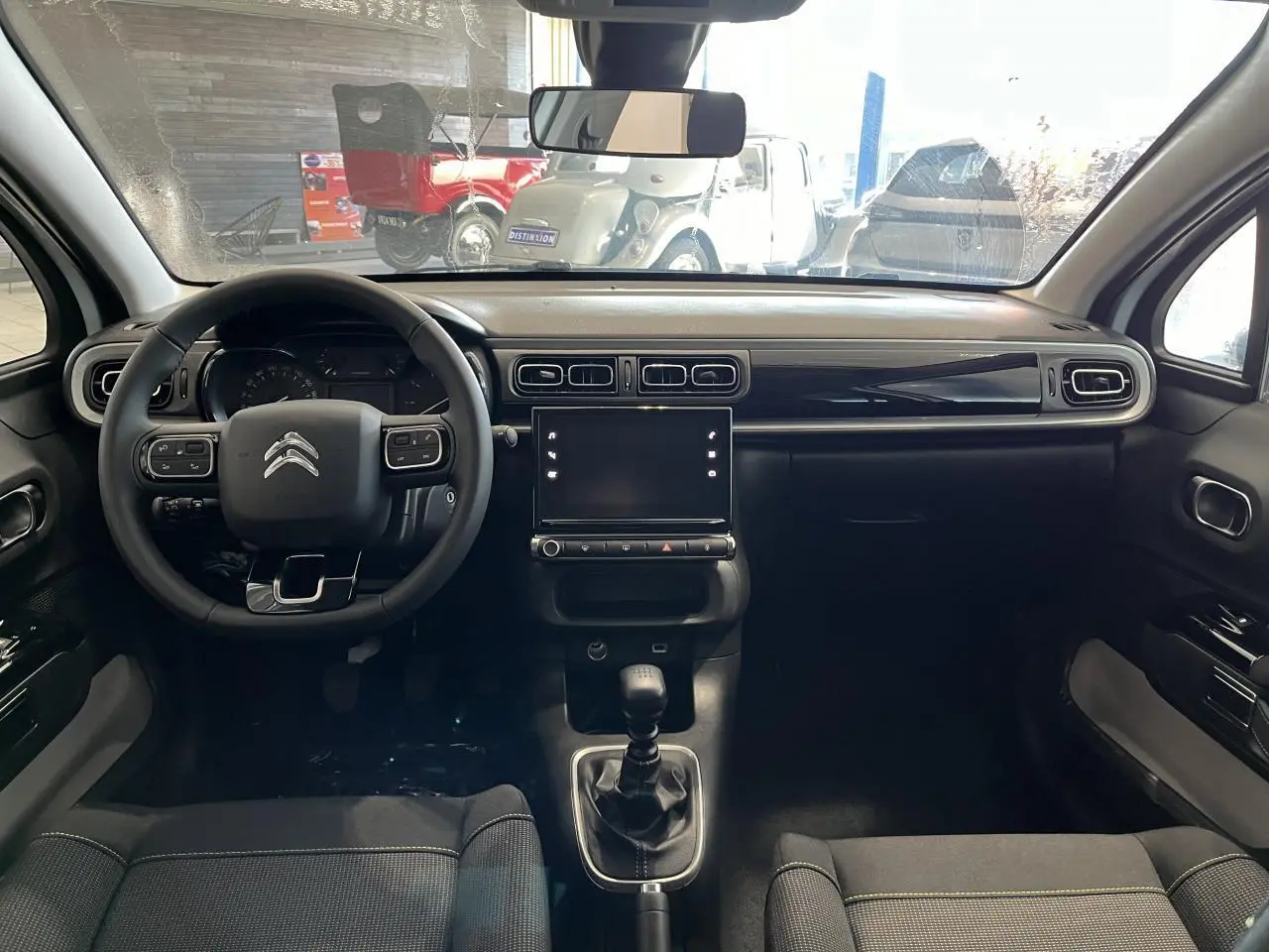 Intérieur de la Citroën C3 2024 vu de face, tableau de bord noir brillant avec écran tactile et volant multifonction.
