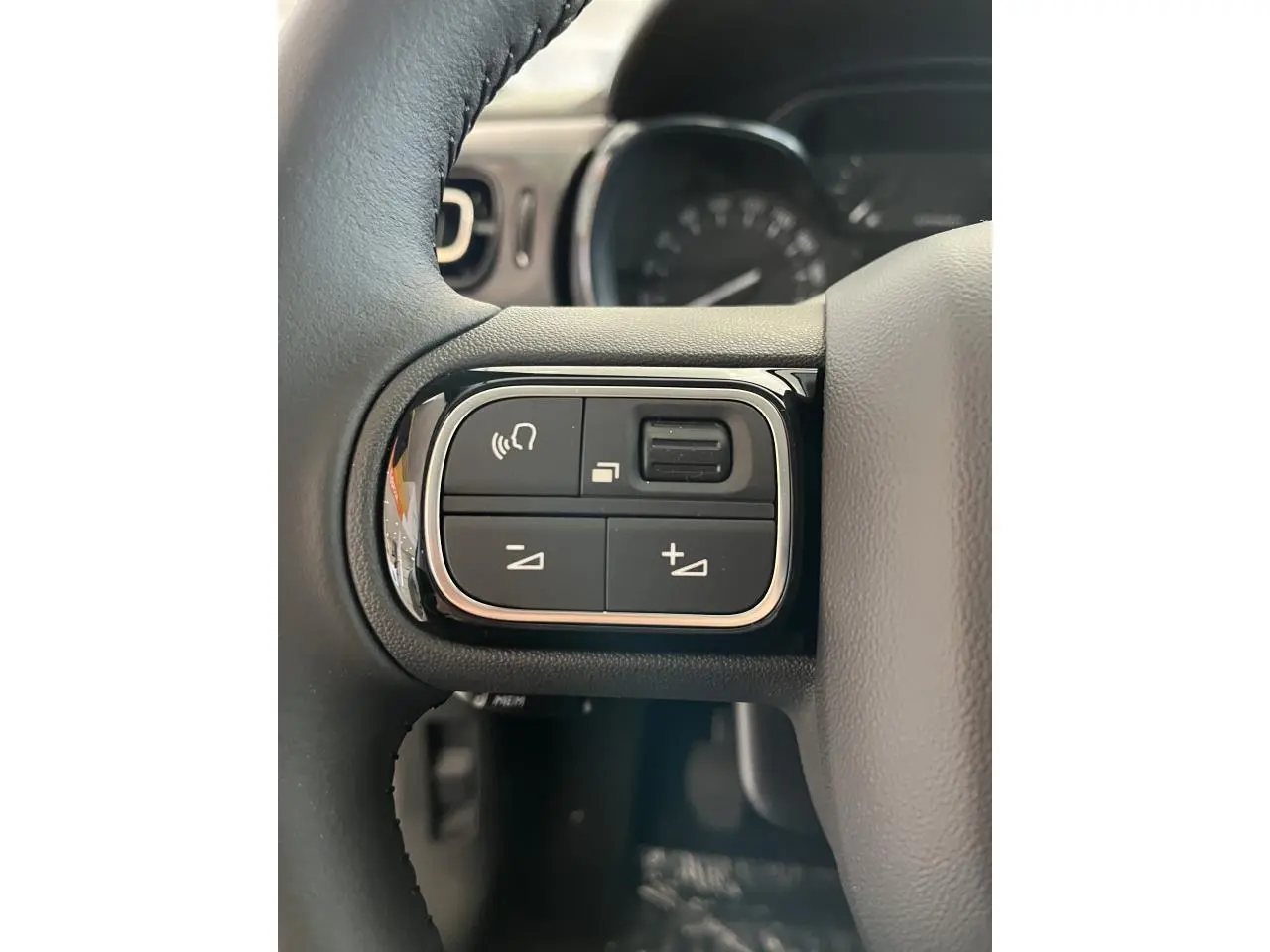 Gros plan sur les commandes audio au volant noir de la Citroën C3 blanche 2024, avec cadrans en arrière-plan flous.