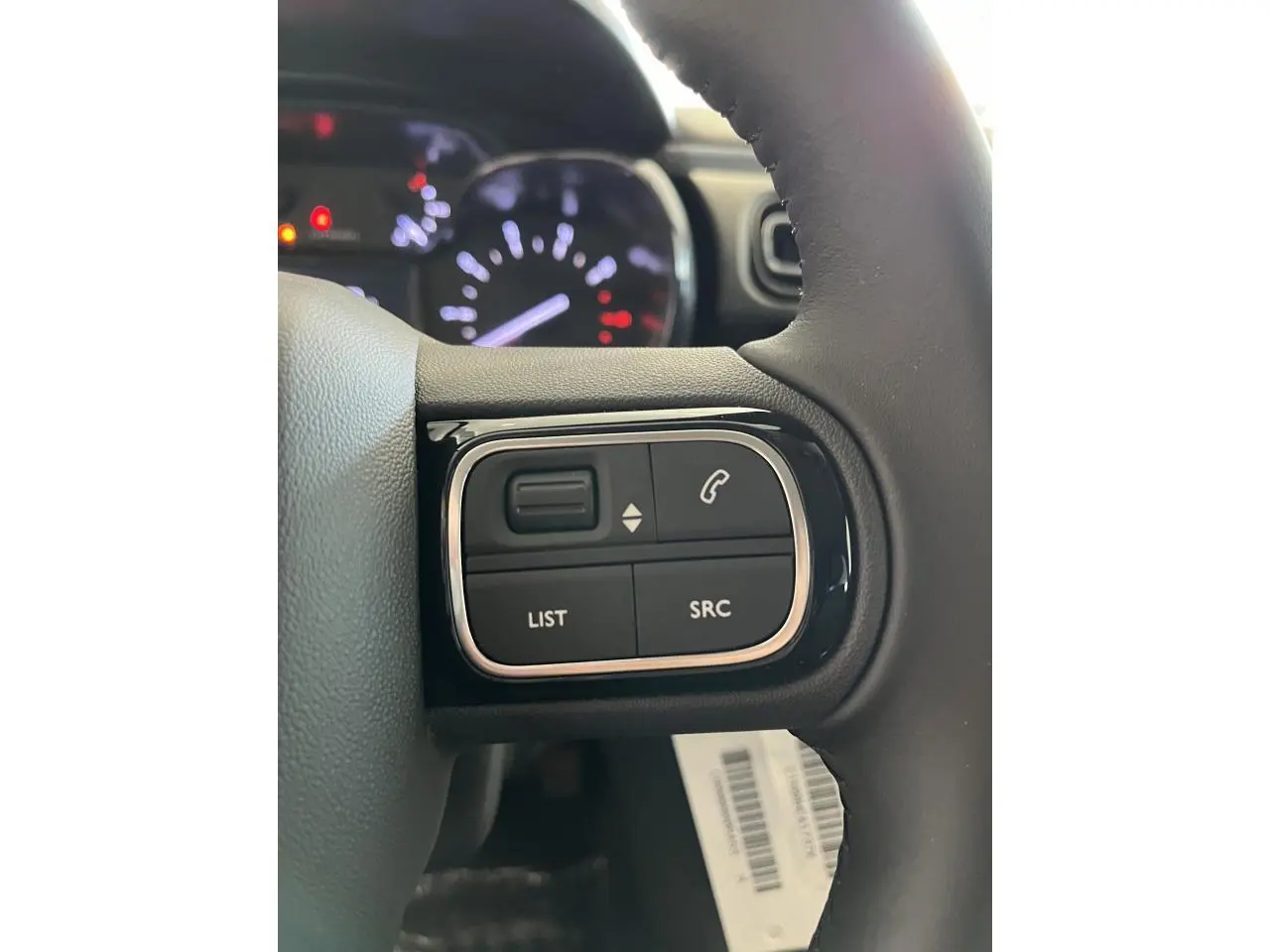 Gros plan sur les commandes audio au volant noir de la Citroën C3 2024, avec tableau de bord flou en arrière-plan.