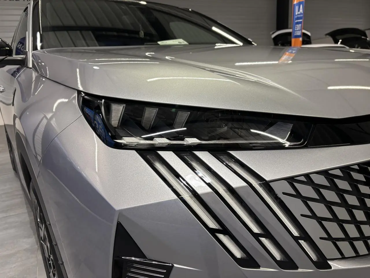 Gros plan sur l’avant droit du Peugeot 3008 gris Artense, mettant en valeur ses phares LED et sa calandre noire laquée.