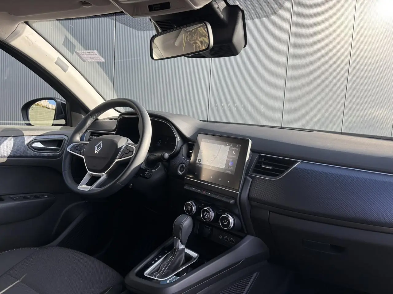 Vue intérieure côté conducteur du Renault Arkana gris métallique, mettant en valeur le volant, l'écran tactile GPS et la console centrale.