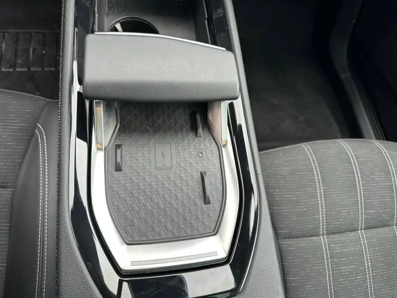 Vue plongeante sur la console centrale noire du Renault Austral 2025, avec tapis de recharge sans fil et accoudoir gris.