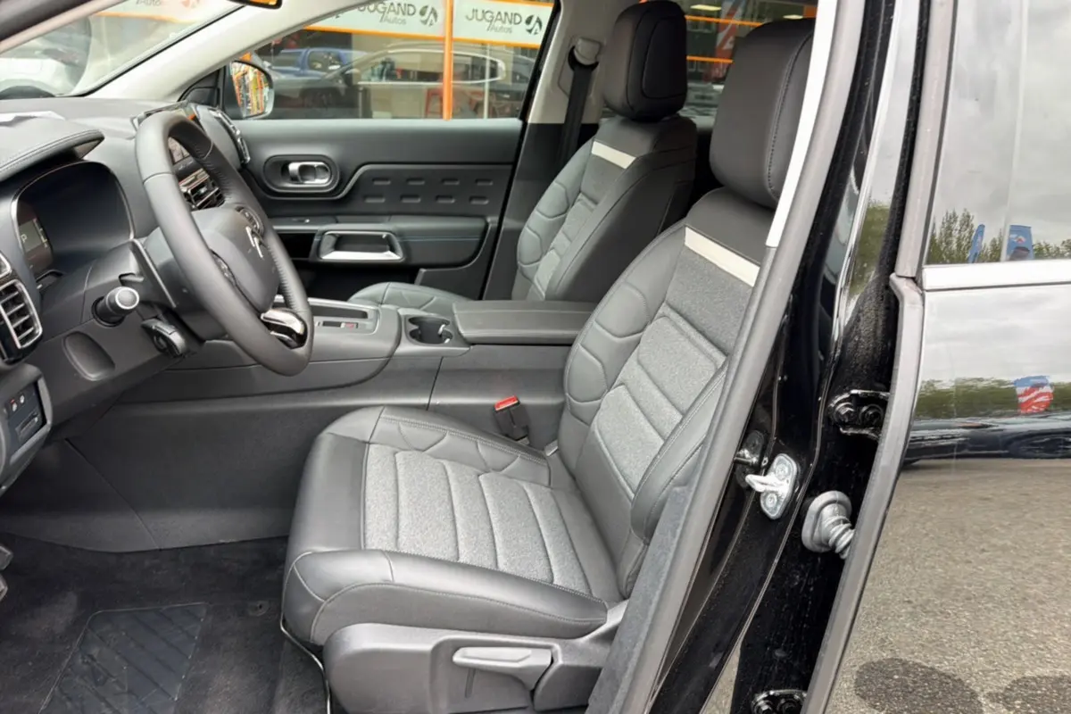 Vue intérieure côté conducteur d’un Citroën C5 Aircross noir 2025, sièges cuir et tissu gris avec console centrale et volant multifonctions.