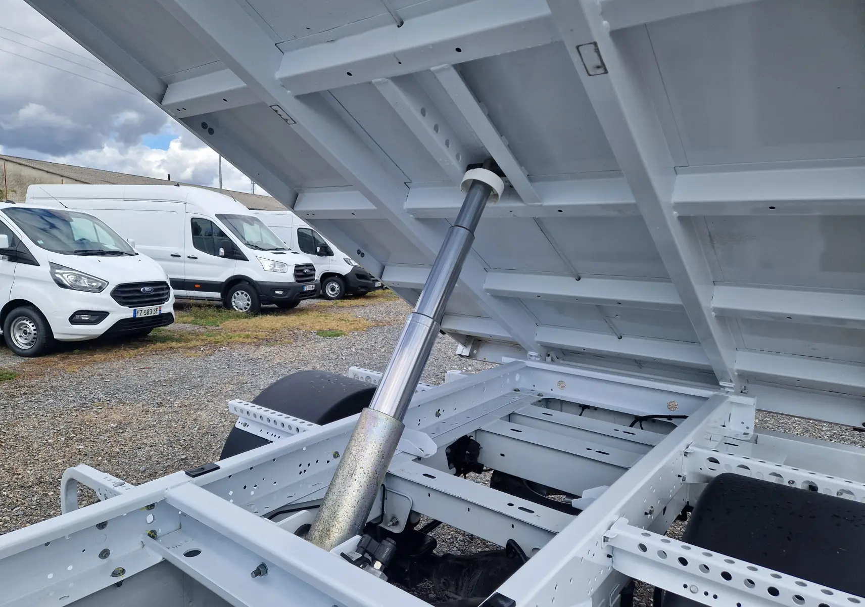 Vue rapprochée sous la benne relevée du Renault Master Châssis Cabine blanc, montrant le vérin hydraulique et le châssis.