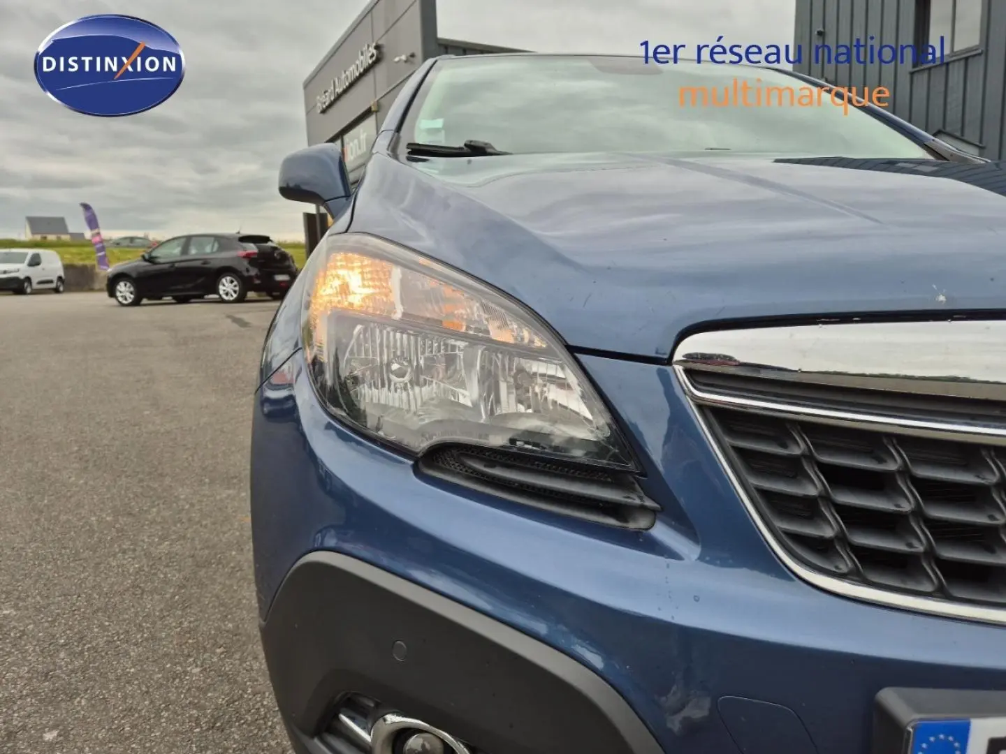 Gros plan sur l'avant gauche bleu outremer de l'Opel Mokka 2015 avec phare allumé et calandre chromée.