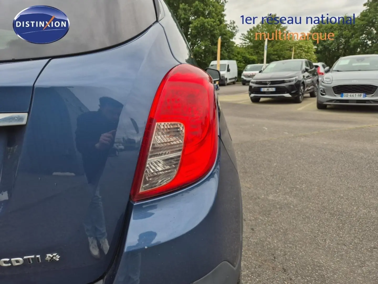 Gros plan sur le feu arrière droit d’un Opel Mokka bleu outremer, avec partie arrière et parking en arrière-plan.