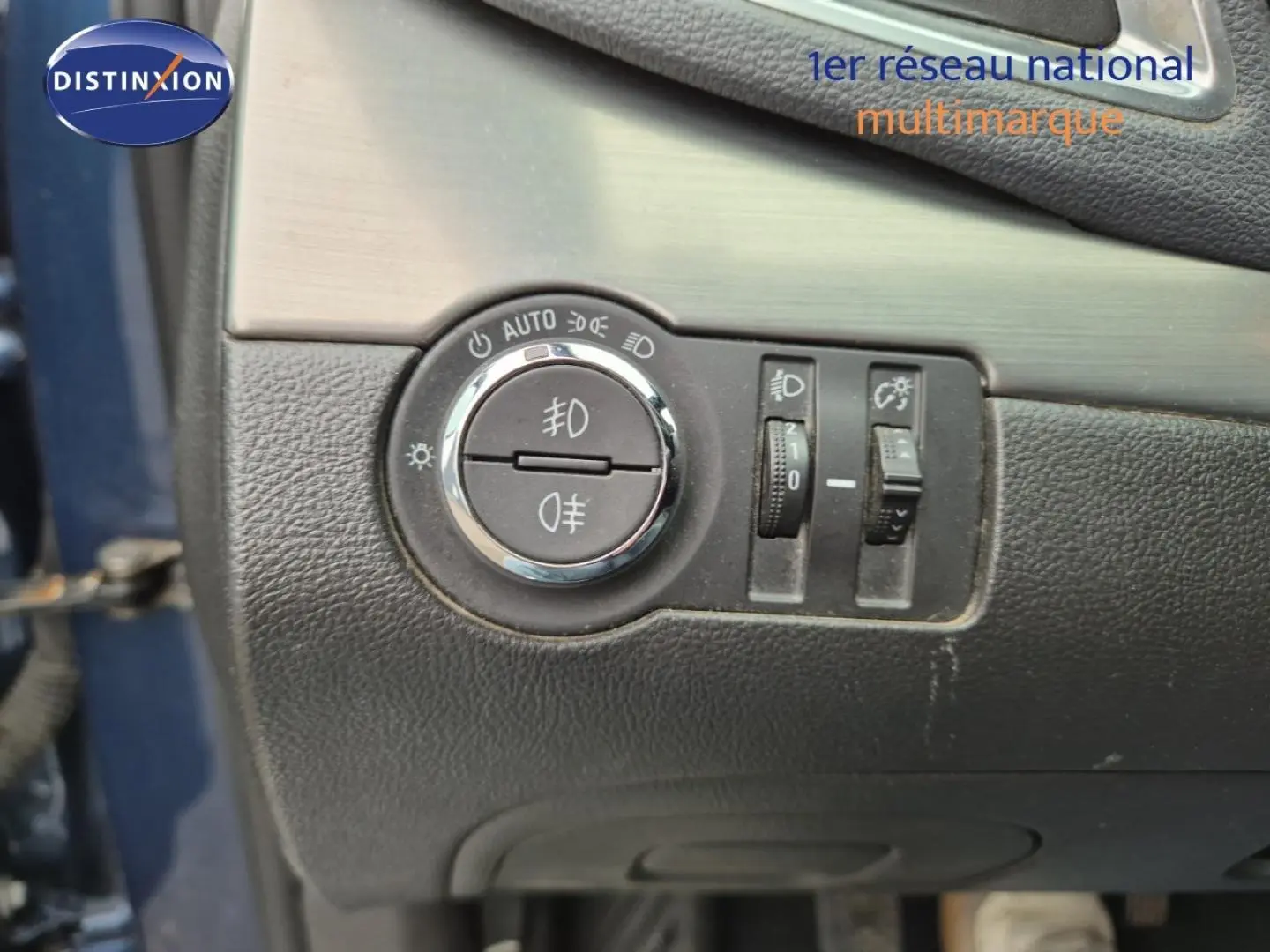 Détail des commandes d’éclairage sur panneau noir intérieur, porte bleu outremer partiellement visible, Opel Mokka 2015.