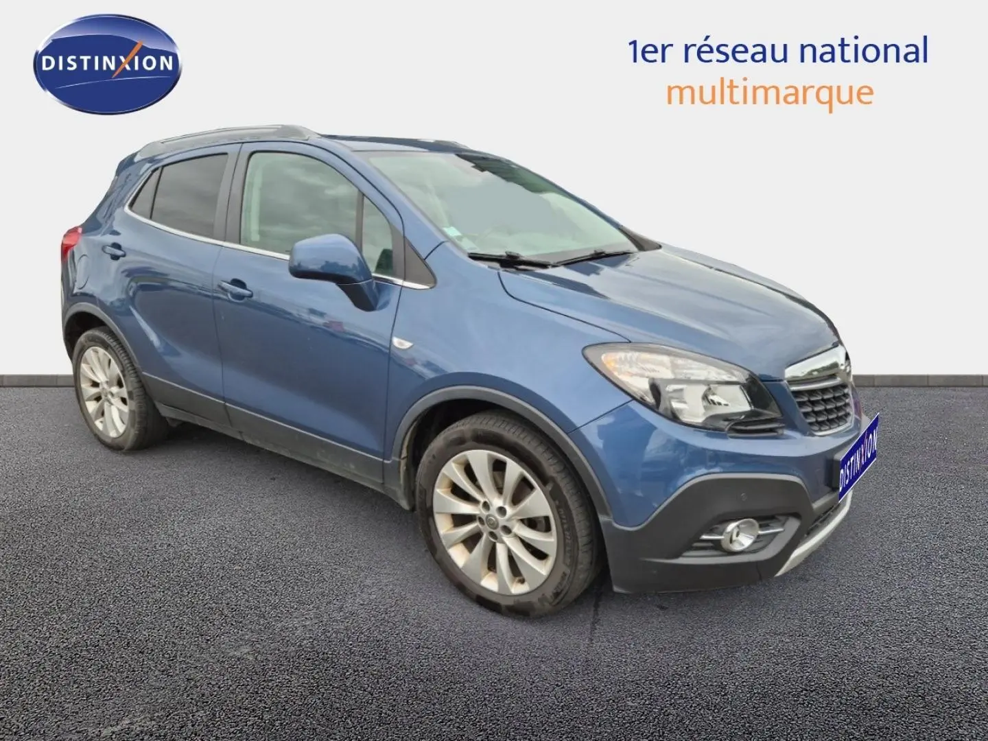 Opel Mokka bleu outremer en 3/4 avant droit, avec jantes alu et barres de toit visibles.