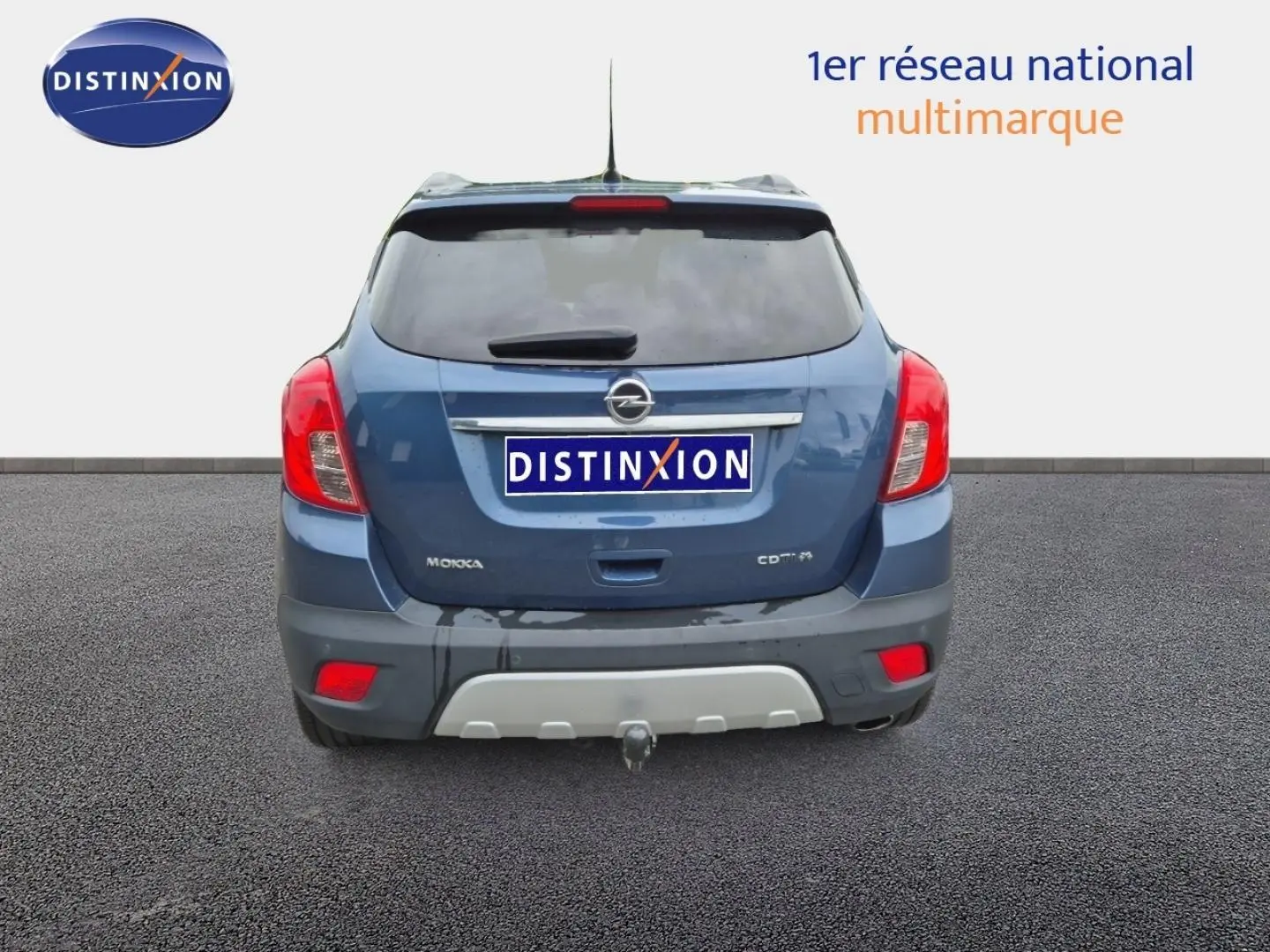 Vue arrière d'un Opel Mokka bleu outremer avec attelage et feux arrière rouges visibles sur fond neutre.
