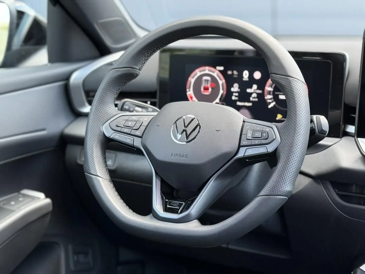 Gros plan sur le volant sport en cuir noir du Volkswagen T-Roc 2026 avec tableau de bord numérique en arrière-plan.