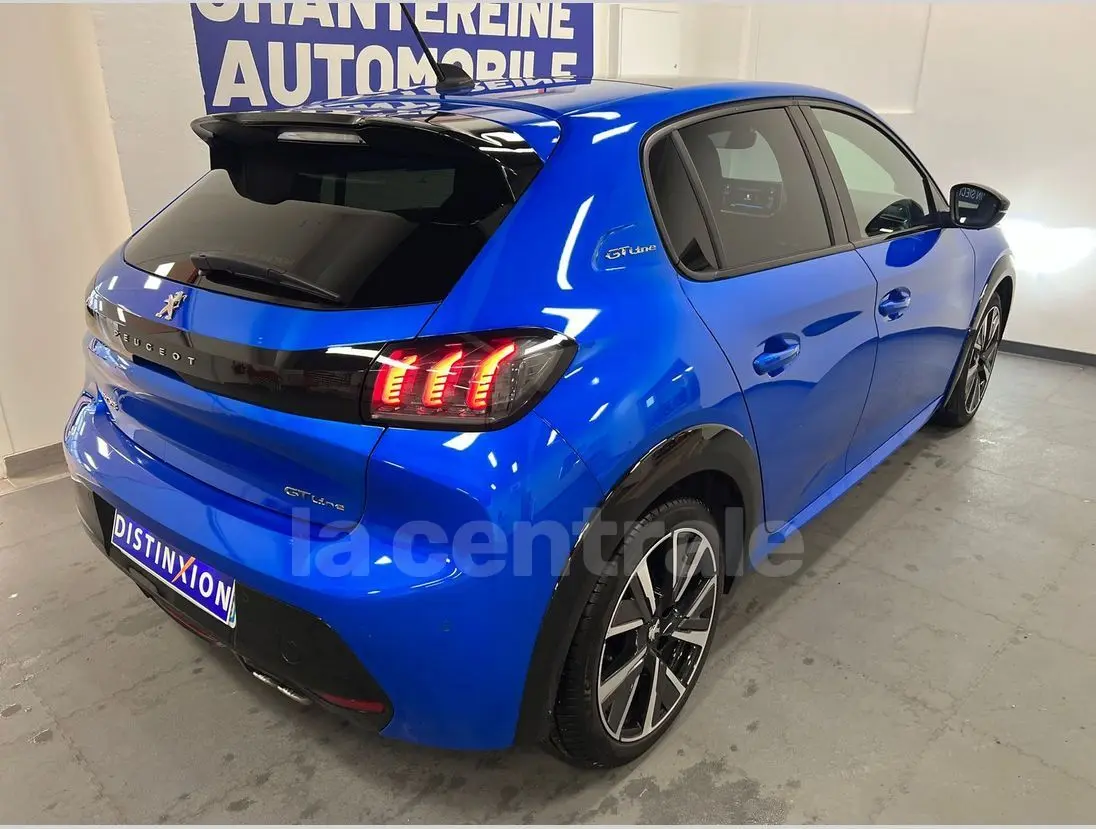 Vue 3/4 arrière droite d'une Peugeot 208 GT Line bleue de 2020 avec feux arrière allumés et jantes alliage noires.