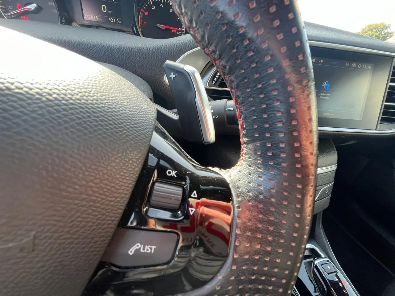 Gros plan sur le volant cuir noir à surpiqûres rouges de la Peugeot 308 SW GT Line avec commandes intégrées et écran tactile visible.