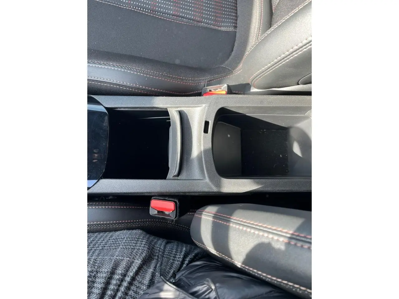 Gros plan sur la console centrale noire avec surpiqûres rouges et sièges en tissu gris foncé de la Peugeot 308 SW GT Line.