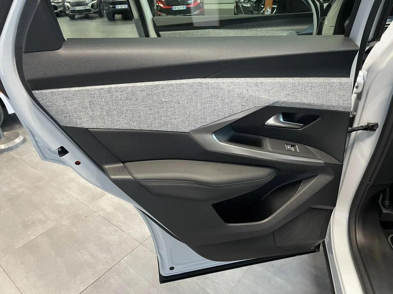 Porte arrière gauche ouverte du Peugeot 3008 blanc Okenite, montrant le décor tissu gris chiné et les commandes de vitre.